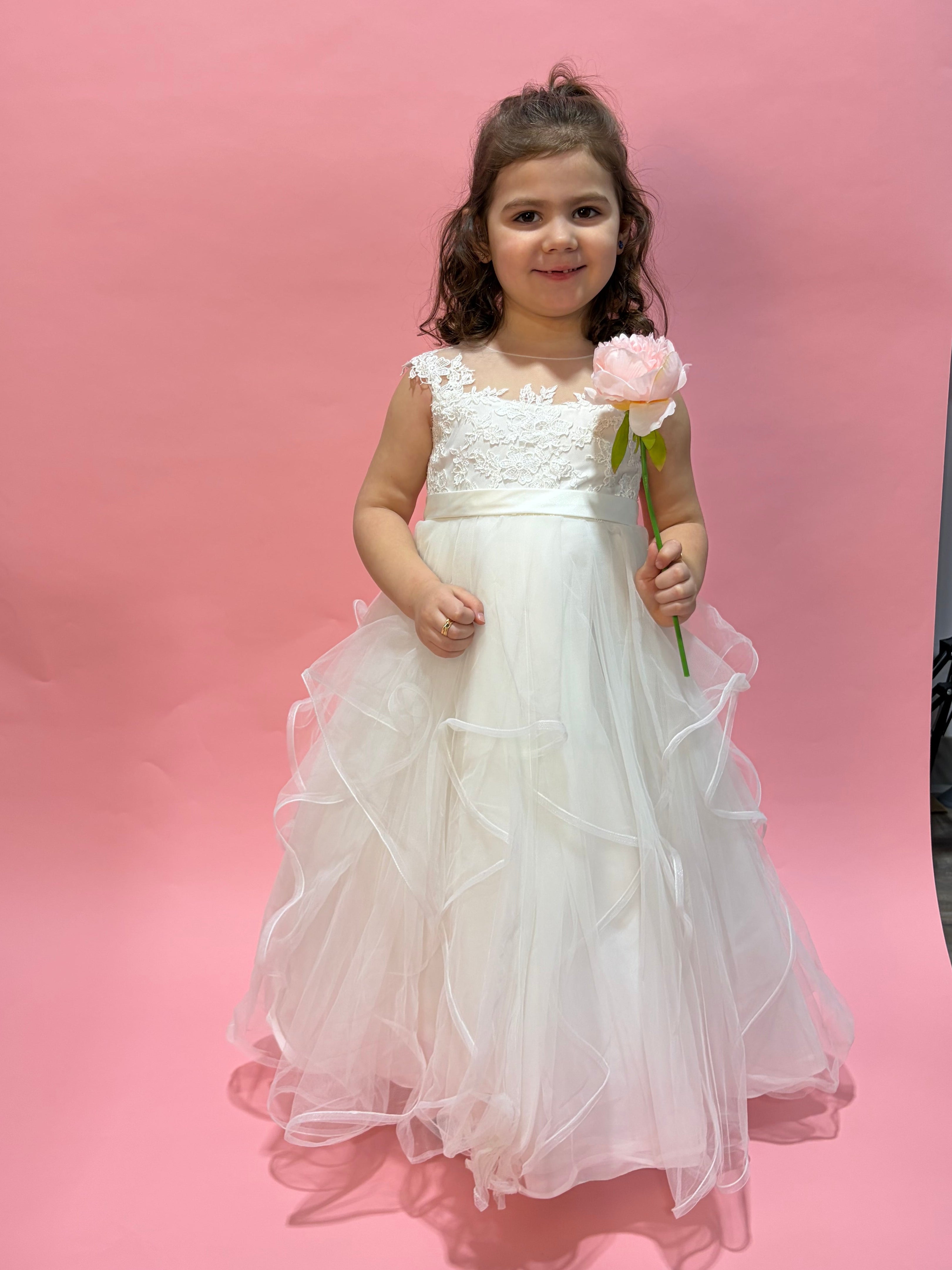 Young girl in a white dress holding flowers against a pink backdrop